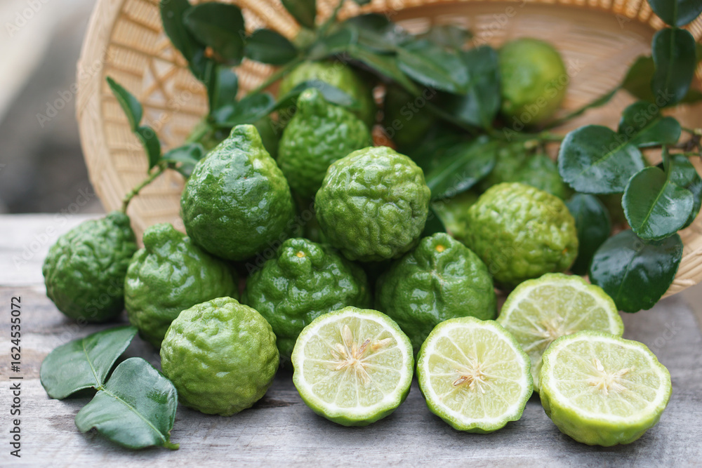 Fototapeta premium Fresh kaffir limes fruits with leaves in basket. Aromatic Thai herb is used for cooking, natural shampoo and homemade cleaners. Known for its citrusy fragrance and traditional medicinal properties.