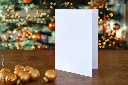 Standing blank empty rectangular greeting card mock up with Christmas balls and before a blurred christmas tree with copy space. For use as a Christmas background template.	