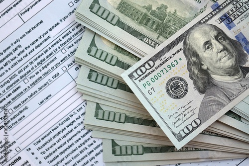 Big amount of United States USD dollar bills banknotes on table with 1040 tax return form