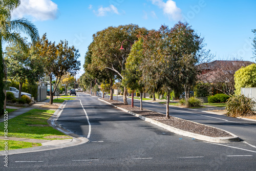 Photos Tree-lined suburban street in a quiet residential neighborhood of Tarneit, Melbourne, Australia, featuring a landscaped central median strip planted with native trees and mulch
