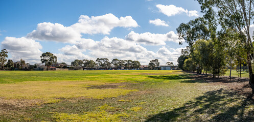 Expansive public reserve in suburban Melbourne Australia, featuring a grass field bordered by native eucalyptus trees under sky. A spacious, quiet, versatile environment for recreation, local sports.