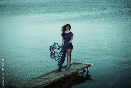 An Elegant Woman Dressed in Blue Graces the Serene Waterside, Capturing Beauty and Charm