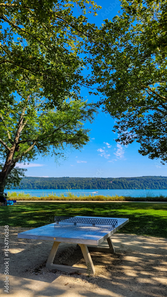 Obraz premium Stationary table to play ping-pong for free in the park of Uberlingen in Germany. There is a lake and a motor boat in the background.