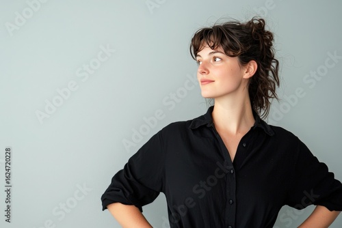Confident Young Woman in Black Shirt Posing Against a Soft Gray Background with a Thoughtful Expression and Natural Light Enhancing her Features