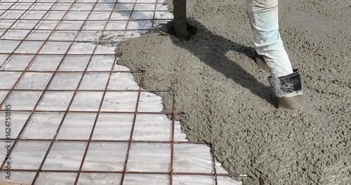 close up of a construction worker in rubber boots standing amidst wet concrete, while a pump hose delivers a fresh pour for a slab directly over a steel rebar grid.