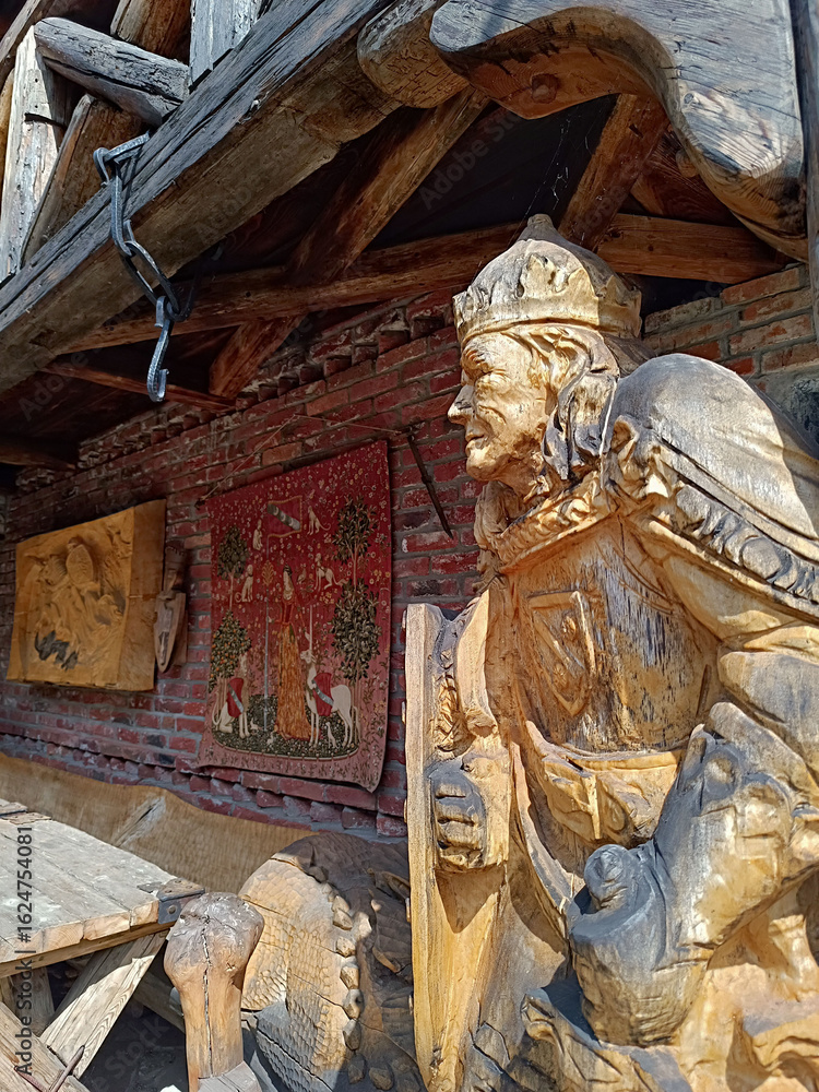 Fototapeta premium Wooden Statue of a Medieval King with Tapestries on a Brick Wall