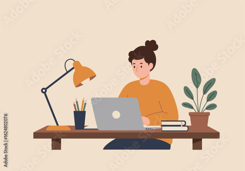 A person with hair in a bun works on a laptop at a desk, accompanied by a lamp, books, and a plant.