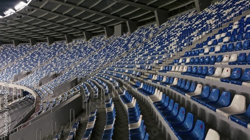 Aerial view drone flies over empty stadium or race track seats. Rows and blue and white seats without viewers and spectators. Evening shot of empty football stadium. Soccer Arena drone aerial view.
