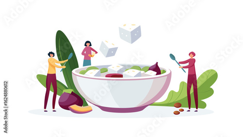 People preparing a salad with feta cheese and vegetables in a large bowl with spoons and leafy greens