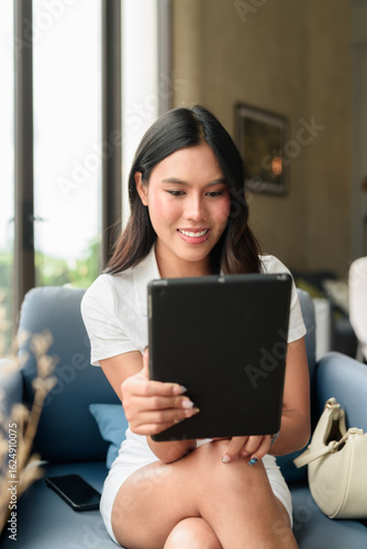 Free Download Young Asian woman in polo shirt using tablet computer indoors in hotel lounge or cafe - GFXLoad