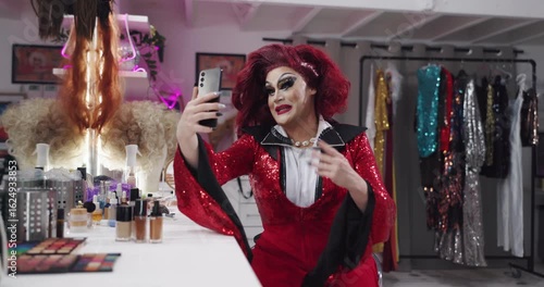 Drag artist, phone and talk with makeup, happy and video call with contact, beauty or chat on web. LGBTQ influencer, person and live stream with cosmetics, excited and social media in dressing room