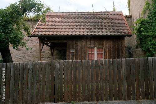 Fotografie Holzschuppen mit Biberschwanzdach vor mittelalterlicher Mauer