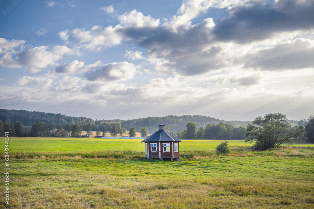 Obraz premium Small red building in a field with mountains in the background