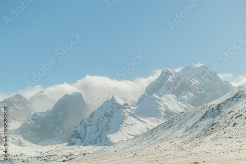 Fotografía A panoramic view of a massive, snowcapped mountain range with clouds swirling ar