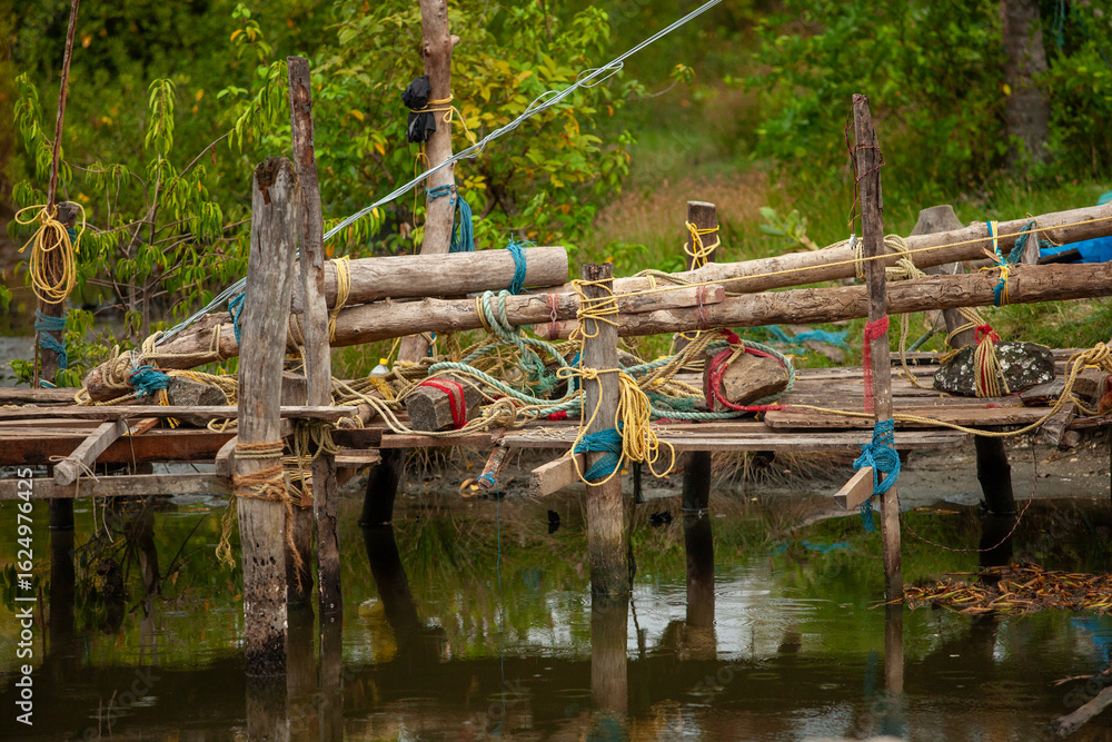 Fototapeta premium Hand-built wooden pier with ropes and rocks in a shallow river, a rustic and textured image for designers needing authentic, natural, or travel-themed visuals for a blog, website, or social media post