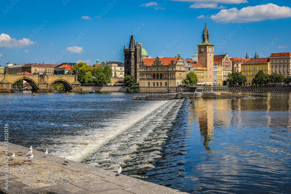 Fototapeta premium Charles Bridge and Old Town buildings in Prague, Czech Republic, with a view of the weir on the Vltava River and seagulls on the riverbank.
