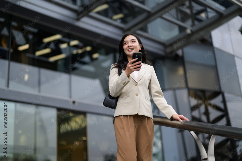 Fototapeta premium Smiling businesswoman using mobile phone app in urban business district