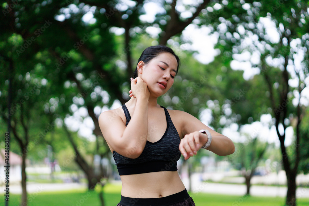 Asian sportswoman suffering neck pain while checking smartwatch during workout in a park Asian sportswoman suffering neck pain while checking smartwatch during workout in a park