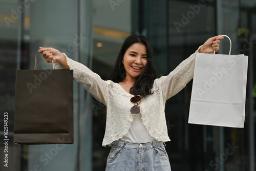 Quadro em tela An Excited Asian female shopper posing with paper bags, smiling with joy after b