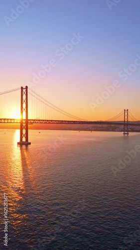 Ponte 25 de Abril Suspension Bridge over Tagus River at Sunset. 25th April Bridge. Portugal. Aerial View. Wide Shot. Drone Moves Forward. Golden Hour. Vertical Video