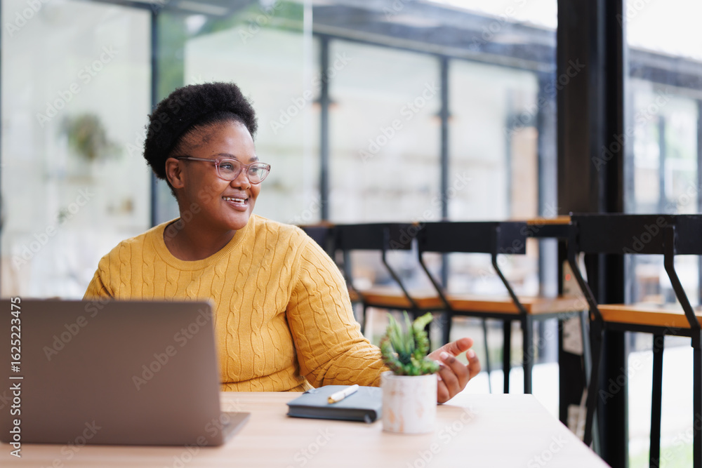Smiling young african american freelancer is working on a laptop in a cafe and talking during a video call, enjoying remote work and flexible schedule Smiling young african american freelancer is working on a laptop in a cafe and talking during a video call, enjoying remote work and flexible schedule