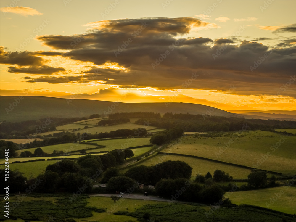 Fototapeta premium Family hiking on Dartmoor tors at sunset, silhouetted against dramatic skies in scenic moorland landscape