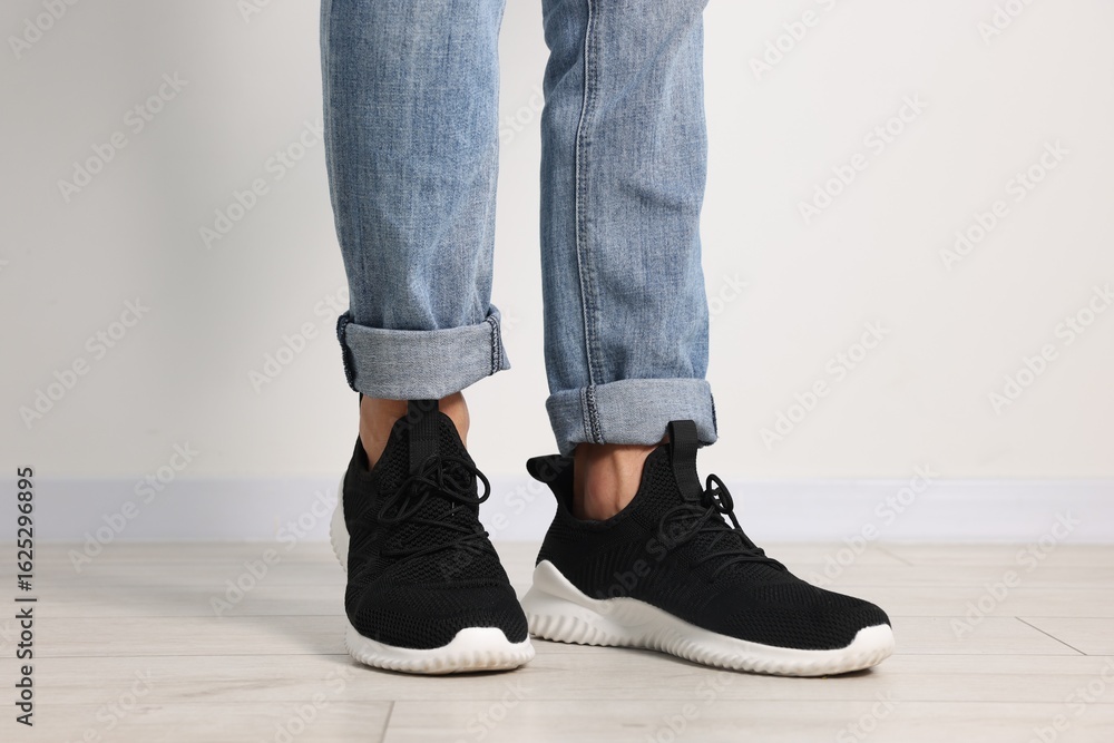 Man wearing pair of black sneakers indoors, closeup Man wearing pair of black sneakers indoors, closeup