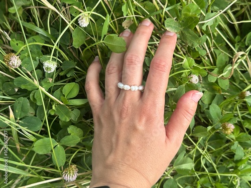 Hand resting on green grass in macro view with pearl ring on finger and natural summer texture