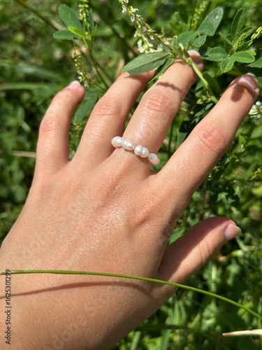Hand resting on green grass in macro view with pearl ring on finger and natural summer texture