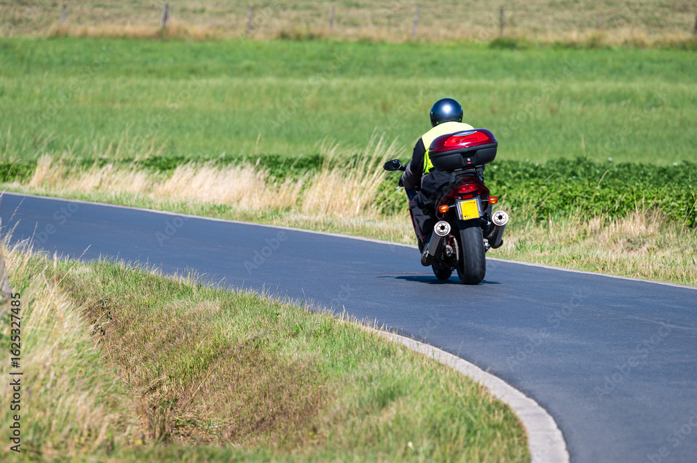 Obraz premium Motorcyclist drving a bending road at the Flemish countryside in Zonnebeke, West Flanders, Belgium