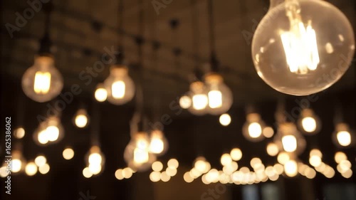 A dark room filled with numerous light bulbs hanging from the ceiling. A few of the bulbs are lit, and the camera slowly pans and zooms, focusing on the illuminated bulbs. As the video progresses.