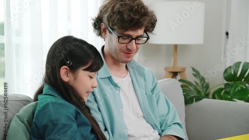 Wallpaper Mural Caucasian father and cute daughter reading story book together while sitting at sofa. Happy dad telling story to cute american child to imagination development while having time together. Pedagogy. Torontodigital.ca