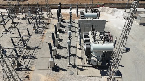 Aerial drone view of an industrial electrical substation with transformers and high-voltage power lines. Infrastructure of the national power grid, captured from above.

