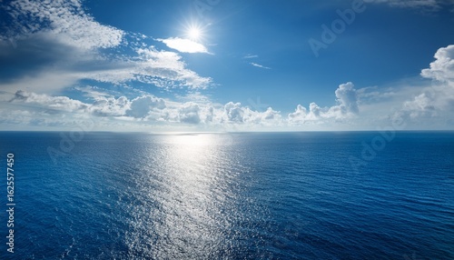 vast ocean under a bright sky with fluffy clouds and sunlight reflection creates a serene atmosphere