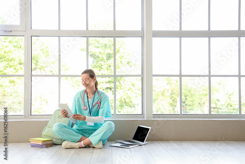 Female medical intern studying with tablet computer near window in clinic