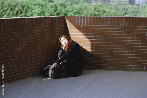 Young Asian woman sitting by brick wall in soft light.