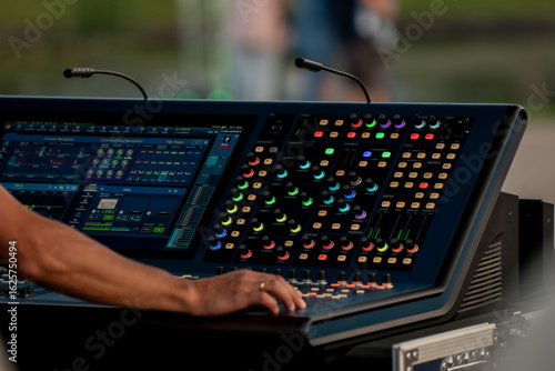 Close-up of professional audio engineer operating colorful digital sound mixing console at live outdoor event, modern stage equipment for concert, broadcast, or technical production use