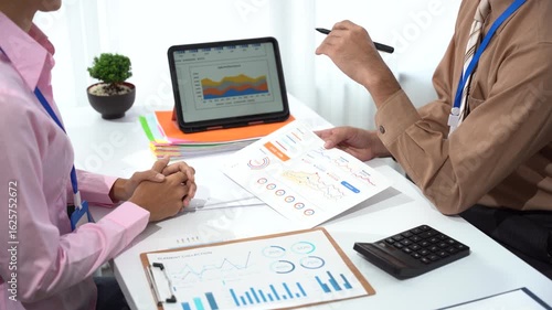 Business Meeting: Two professionals collaborate over financial charts and graphs, analyzing data and strategizing on the business and plan. A focused view that emphasizes strategic discussions. 