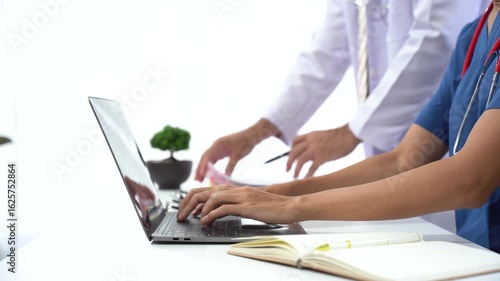 Medical Team Collaboration: A healthcare professional types on a laptop while another stands beside, reviewing documents, capturing the synergy of teamwork in a modern medical setting.