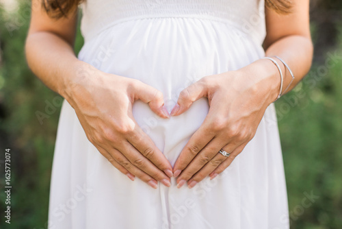 a woman making a heart with her hands on her pregnant belly