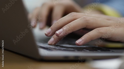 Close-up of young Asian woman's hands, early 20s, typing on laptop in library setting. Represents digital work, education, productivity, and remote study or freelance concepts.