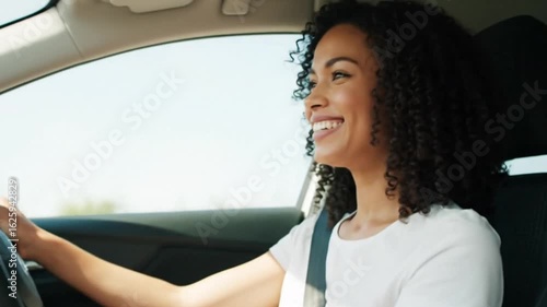 A beautiful young woman with a smile on her face is driving an automobile on the road