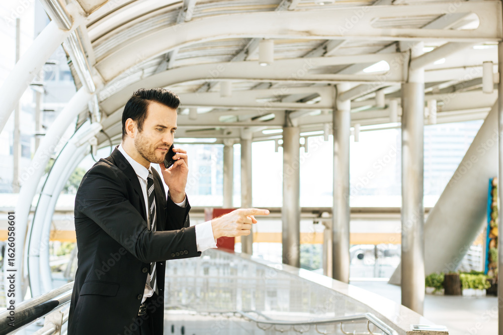 A businessman in a suit stands outside a building talking on the phone with a fierce expression. A businessman in a suit stands outside a building talking on the phone with a fierce expression.