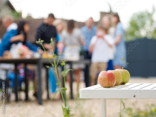 Photos Trois pommes posées sur une table de jardin blanche, en avant-plan d’une scène f