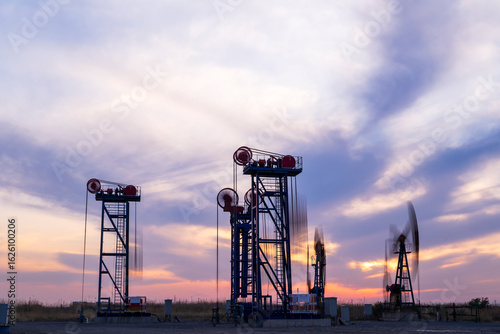 in the evening, oil pumps are running, The oil pump and the beautiful sunset reflected in the water, the silhouette of the beam pumping unit in the evening.