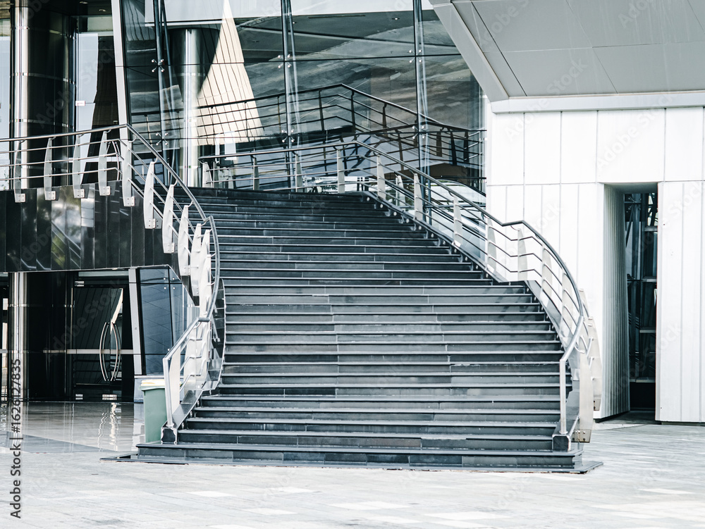 Obraz premium Wide staircase with modern steel railings in a sleek commercial building lobby, highlighting contemporary architecture, symmetry, and urban interior design.