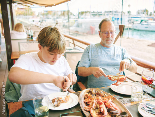 Outdoor portrait of father and teenager son eating seafood in seaside restaurant