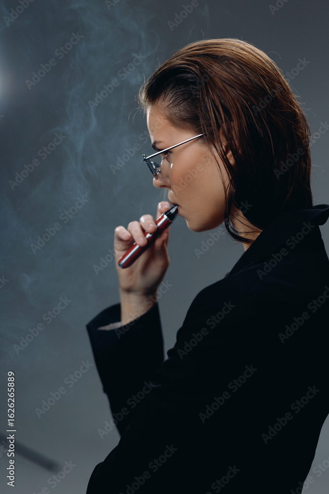 Obraz premium Profile of a young woman vaping indoors with smoke, wearing glasses and dark clothing
