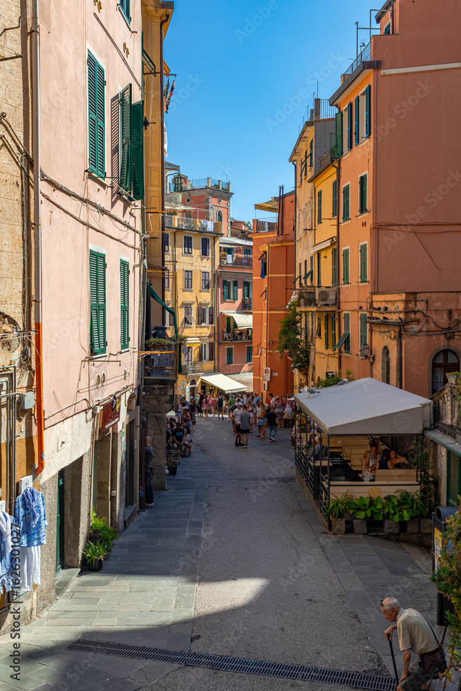 Fototapeta premium A photo of a narrow street with a few people sitting on benches