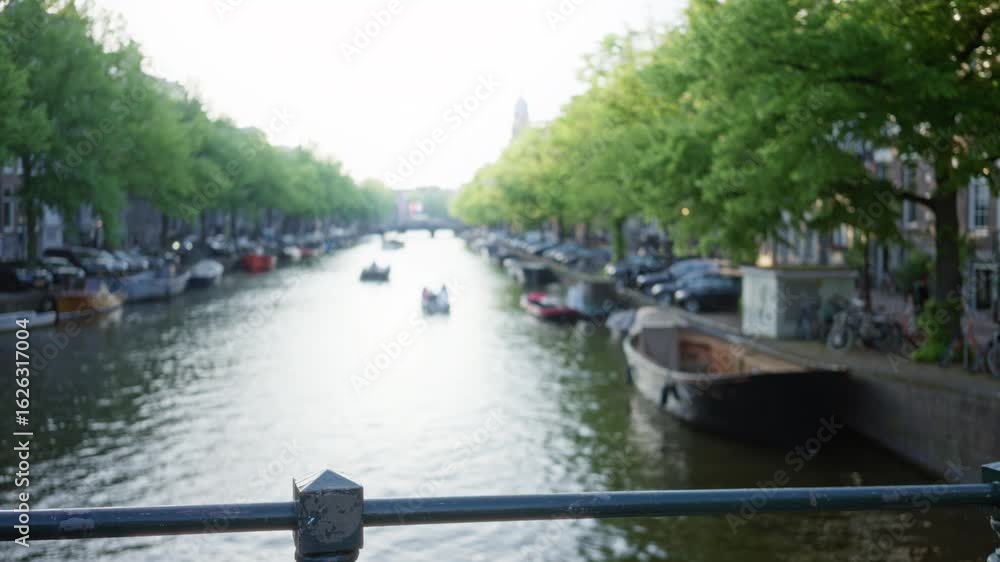 Serene canal in amsterdam with boats and lush trees lining the water, captured with a blurred focus for an artistic effect. Serene canal in amsterdam with boats and lush trees lining the water, captured with a blurred focus for an artistic effect.